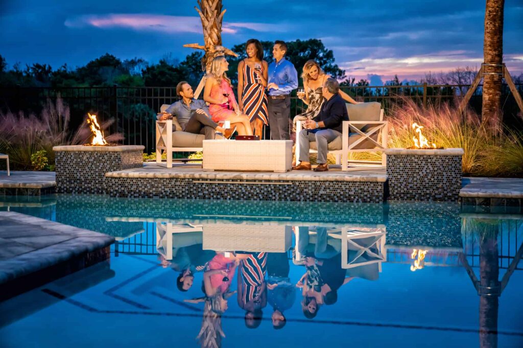 Group of couples sitting together by a poolside fire pit at sunset